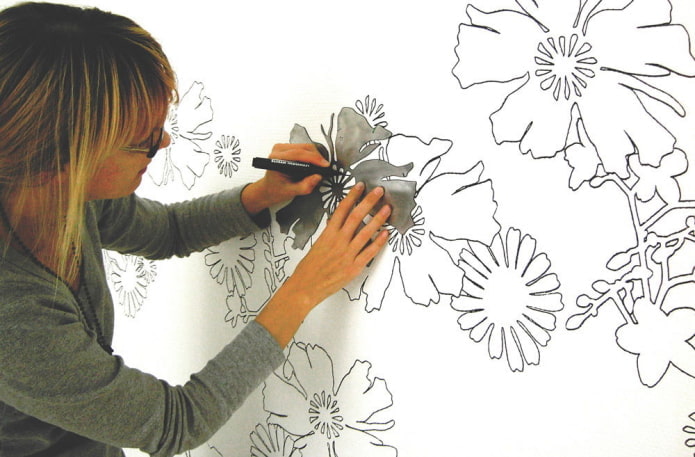 Frau malt Blumen mit einer Schablone an die Wand
